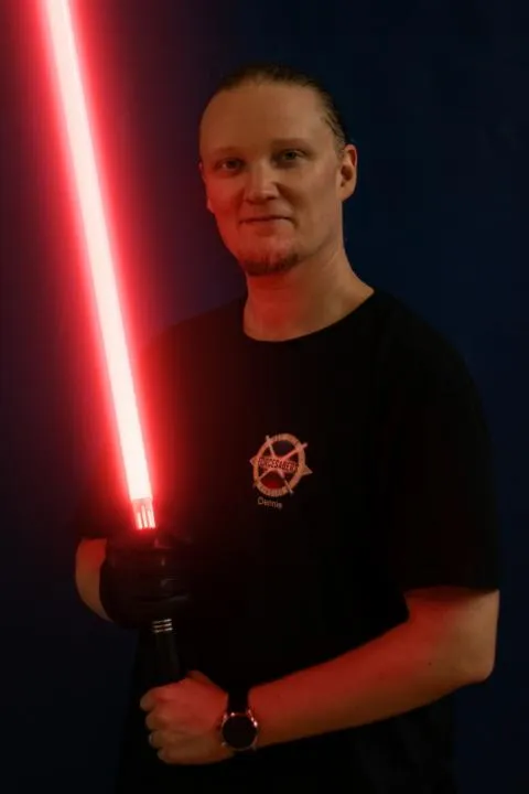 Portrait von Dennie mit einem Lichtschwert in der Hand.